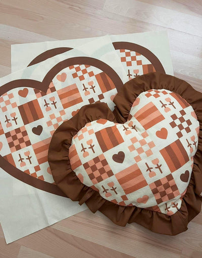 Heart-shaped pillow with checkered pattern and brown border on a wooden surface