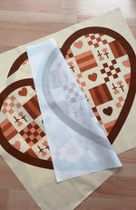 Heart-shaped quilt pattern fabric panel on a wooden surface.