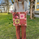 Person holding a quilt with 'Home Sweet Home' text in an outdoor setting