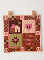 Patchwork wall hanging with 'Home Sweet Home' text and heart designs on a white background