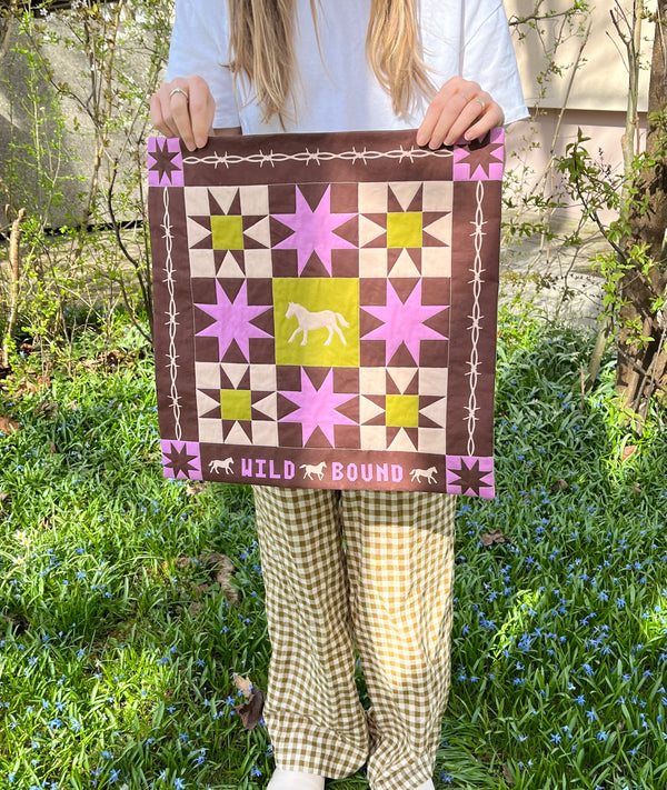 Person holding patchwork style quilted wall hanging outside.